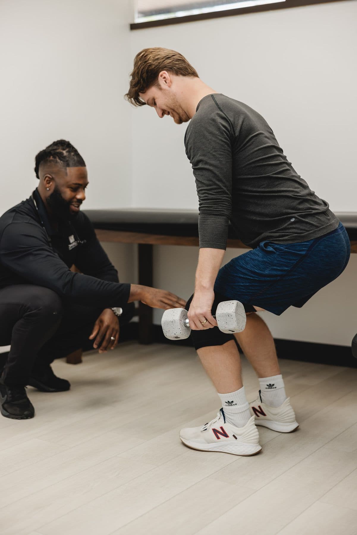 A Chiron physician guiding an adult's squat with a dumbbell
